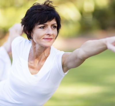 Fit, brunette women, dressed in white clothing, practicing yoga outdoors.