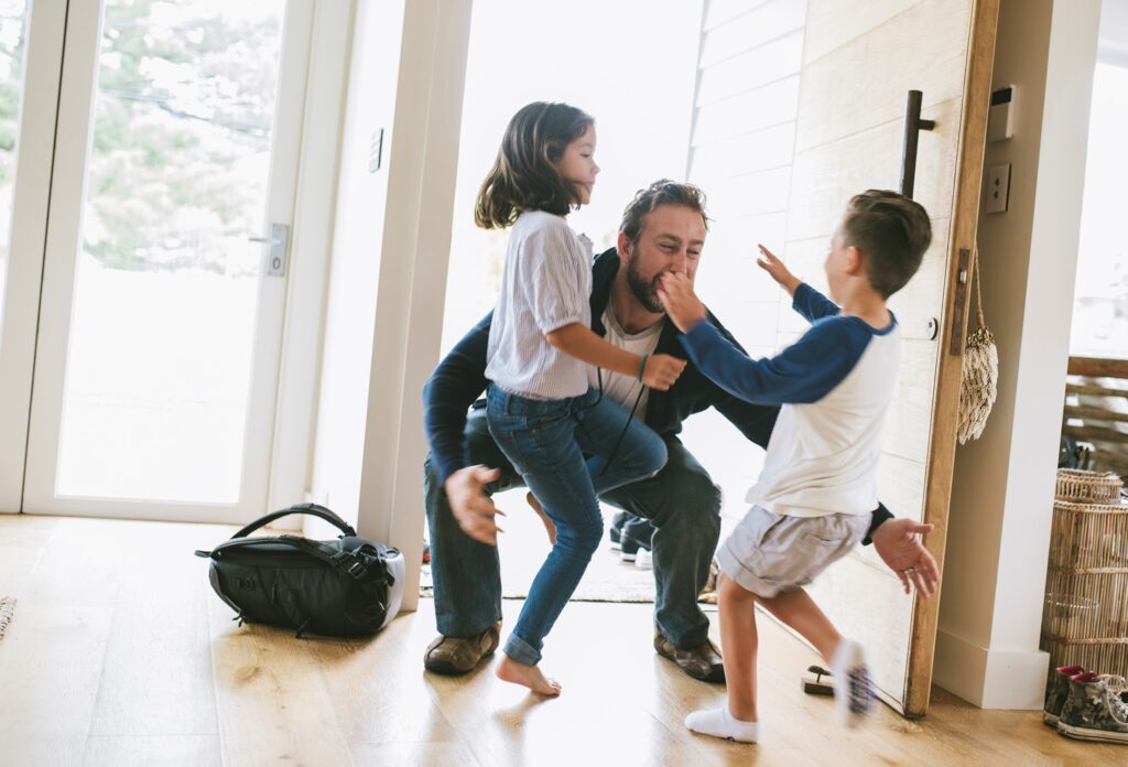 Children running towards their father that just came through front door of their house. One little girl and one little boy. They are happy, smiling.
