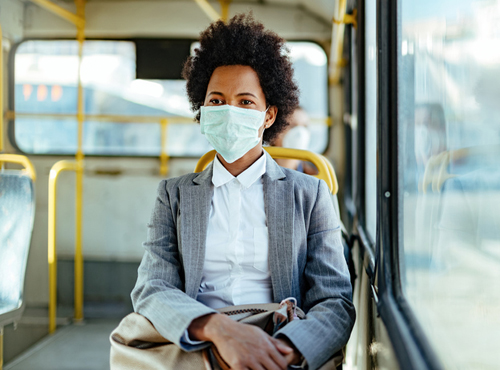 African American businesswoman with face mask for virus protection while commuting by bus.