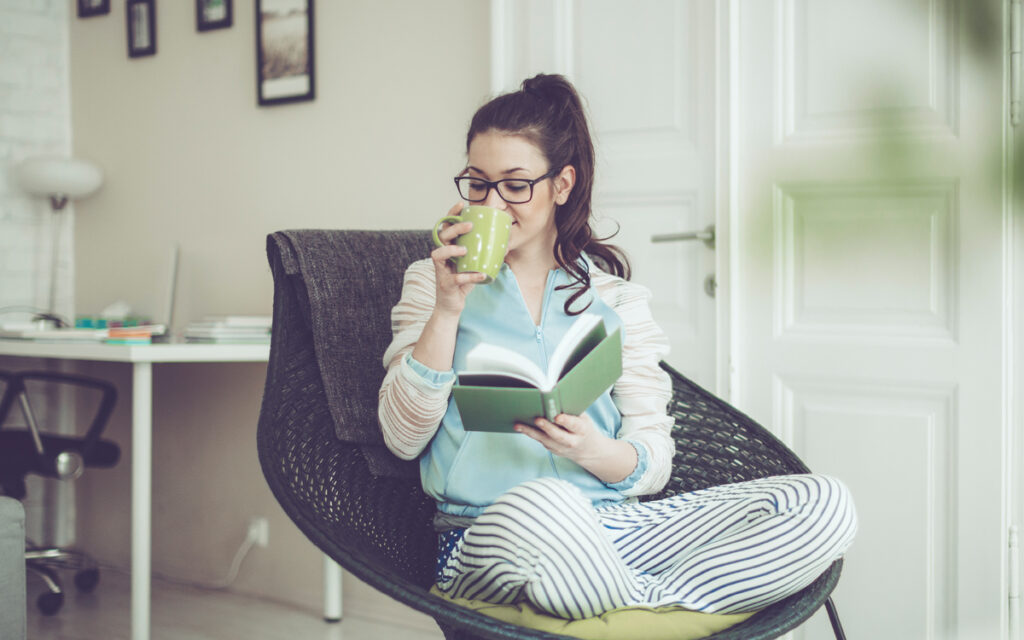 Young woman sipping tea and reading book at home.