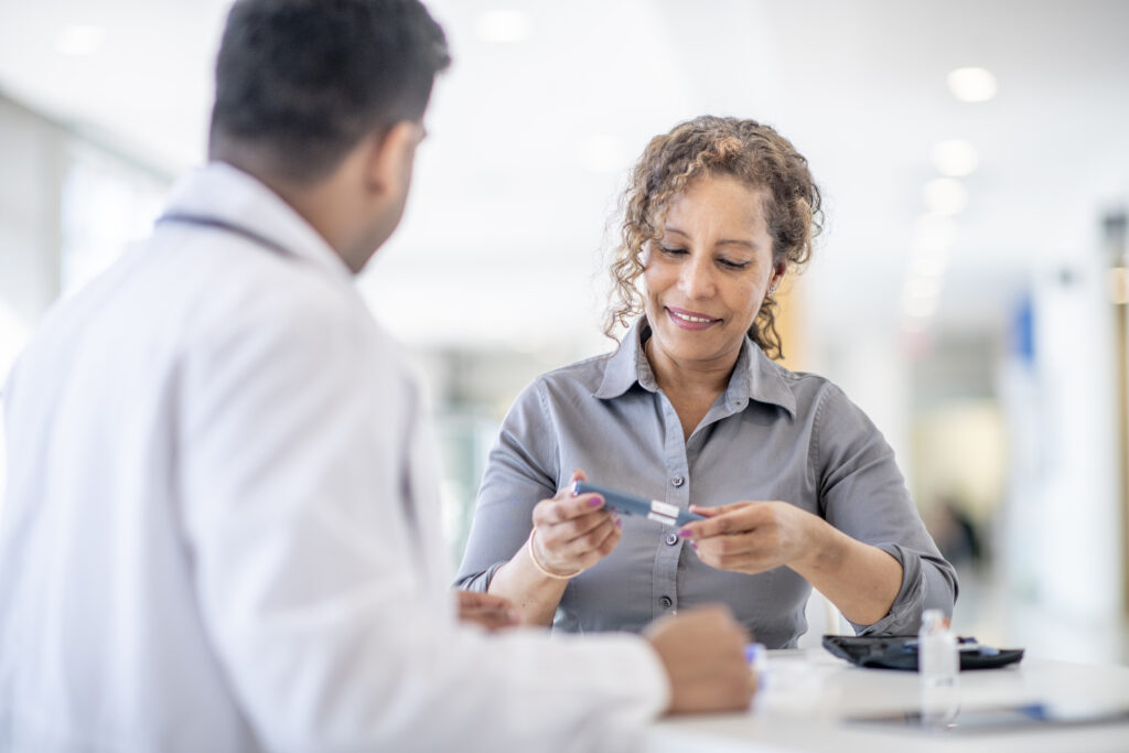 A female adult is at a medical check up appointment for a diabetic medical condition. She is holding a glucometer pen that is used to test her blood sugar levels.