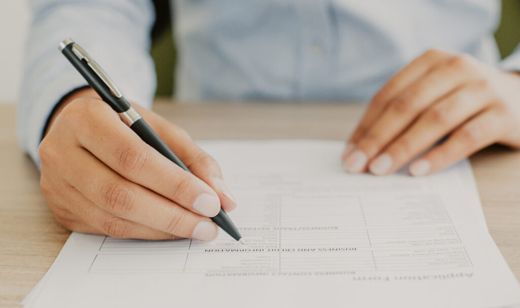 Cropped view of person holding pen and filling out application form on table