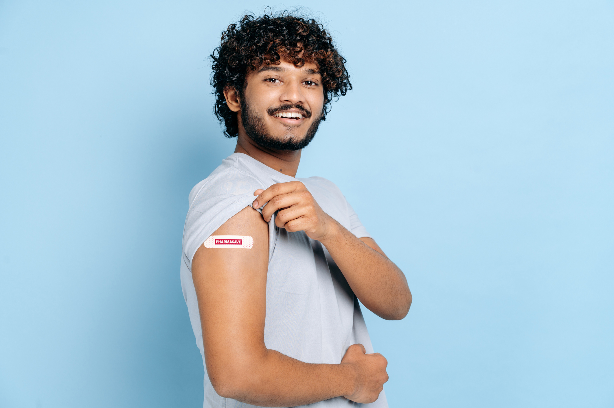 Healthcare concept. Treatment and prevention, vaccination concept. Satisfied indian or arabian man with a band aid on shoulder after vaccination against covid 19, stands on isolated blue background